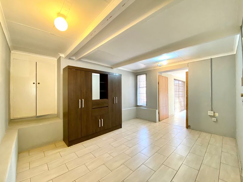 A bedroom featuring tiled flooring, built-in storage, and exposed ceiling beams, leading to an adjacent hallway with a security gate.