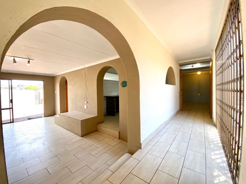 An open-plan living area featuring distinctive architectural archways, tiled flooring, and a built-in platform, offering a versatile space ready for personalization.