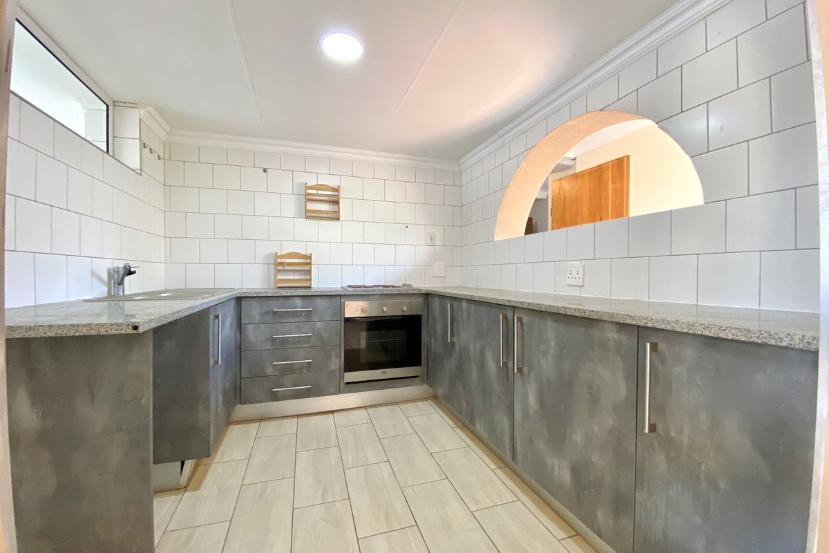 A clean, modern kitchen featuring grey cabinetry, granite countertops, subway tile backsplash, built-in oven, and a unique architectural archway.