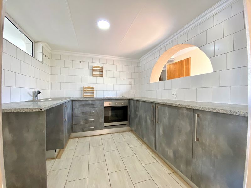 A clean, modern kitchen featuring grey cabinetry, granite countertops, subway tile backsplash, built-in oven, and a unique architectural archway.