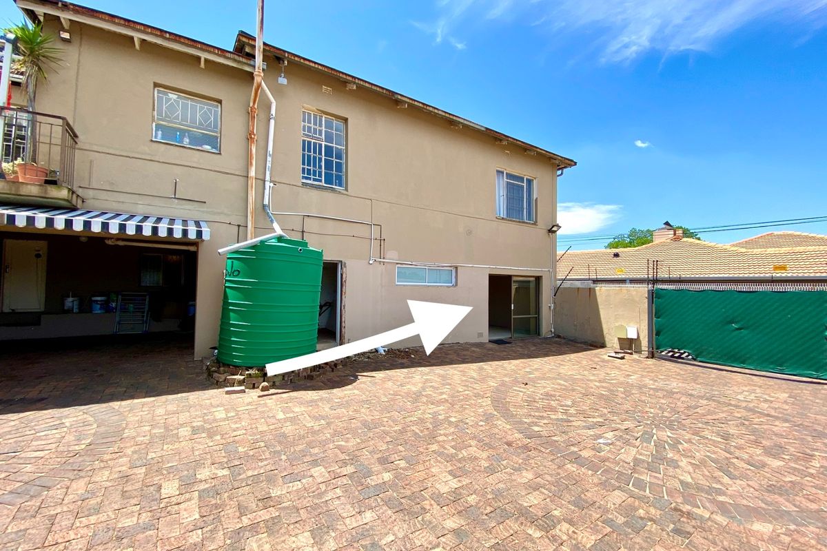 Rear exterior view of the apartment building featuring a paved courtyard, water tank installation, and access to the ground floor unit.