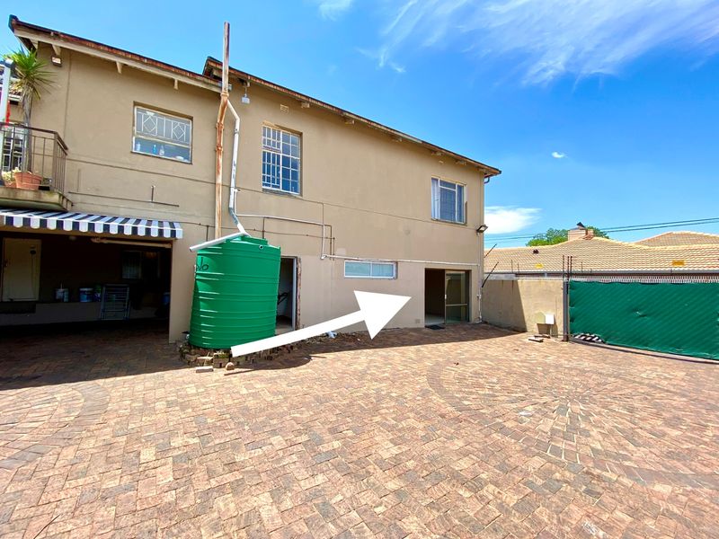 Rear exterior view of the apartment building featuring a paved courtyard, water tank installation, and access to the ground floor unit.