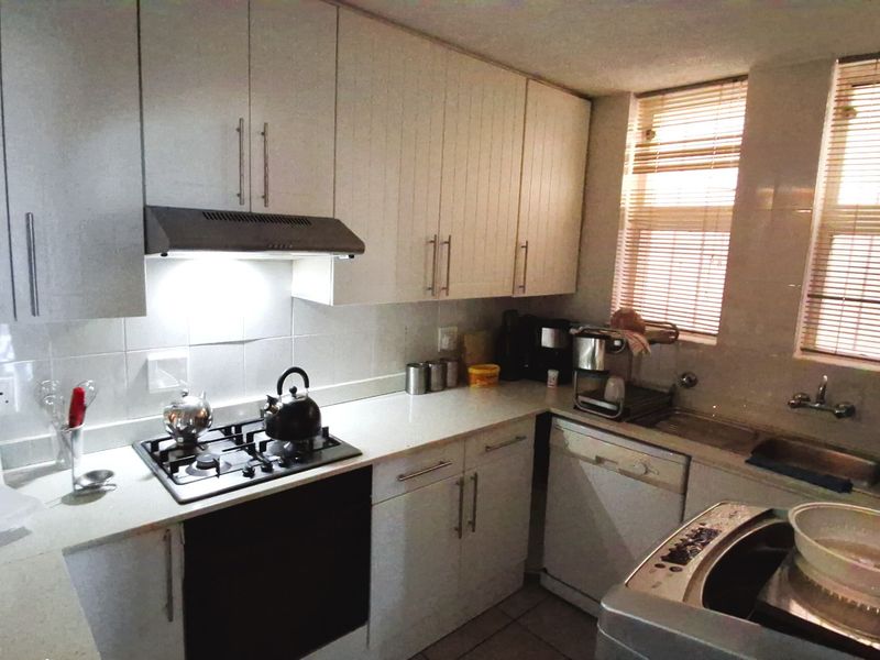 A functional kitchen featuring white built-in cabinetry, a gas hob with extractor fan, tiled backsplash, and a stainless steel sink with window views.