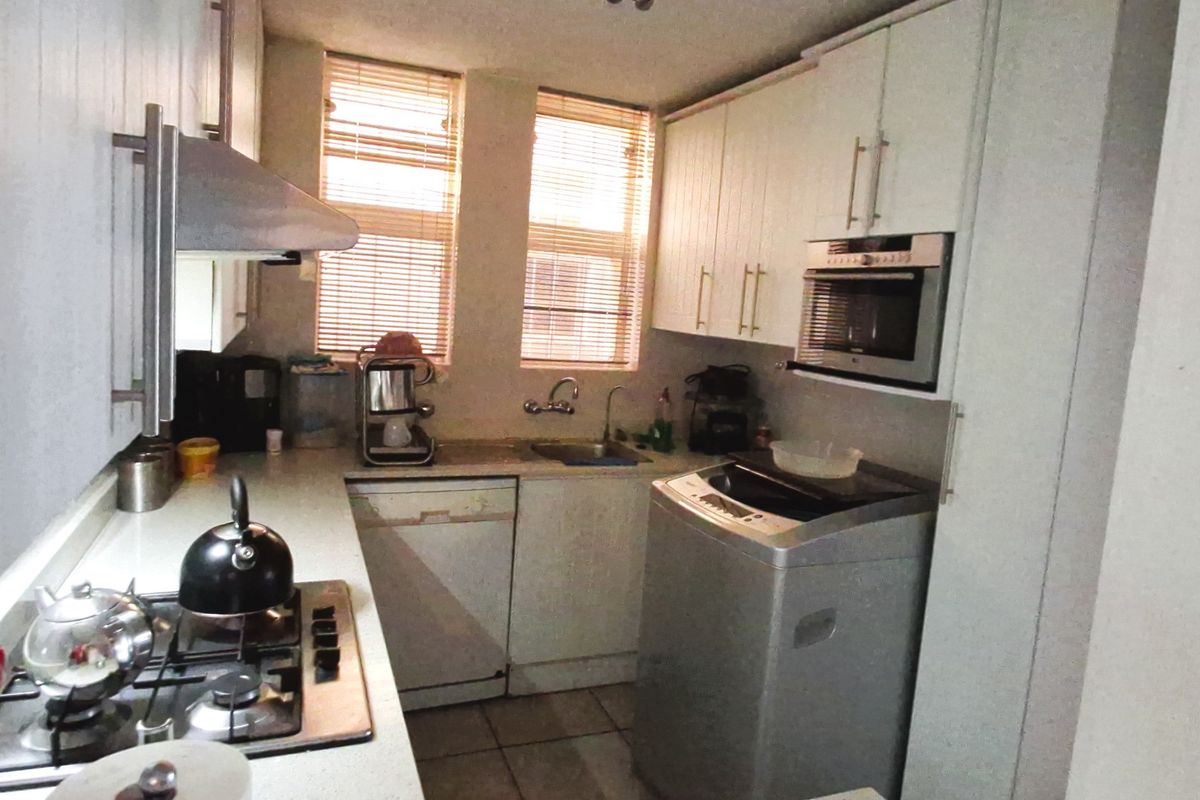 Compact kitchen featuring white cabinetry, gas hob, extractor fan, built-in oven, microwave, and integrated dishwasher with dual windows providing natural light.