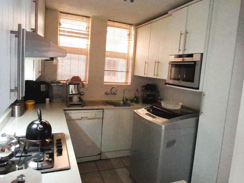 Compact kitchen featuring white cabinetry, gas hob, extractor fan, built-in oven, microwave, and integrated dishwasher with dual windows providing natural light.