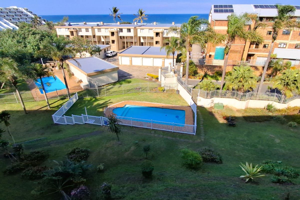 An elevated aerial view of the apartment complex grounds, featuring a communal swimming pool, landscaped garden areas, and secure garage facilities.
