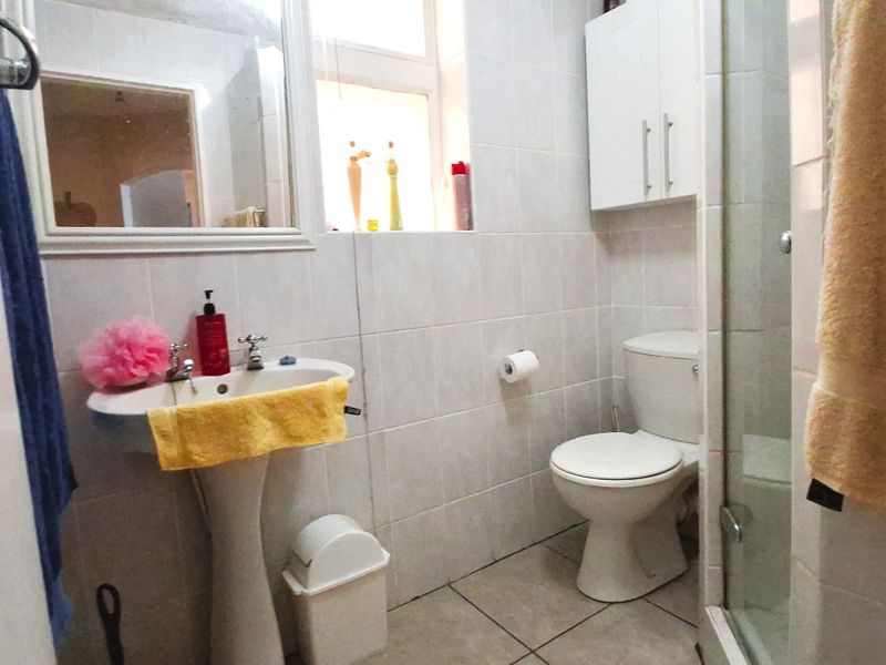 A functional bathroom featuring a pedestal basin, toilet, and a glass-enclosed shower with neutral wall and floor tiling.