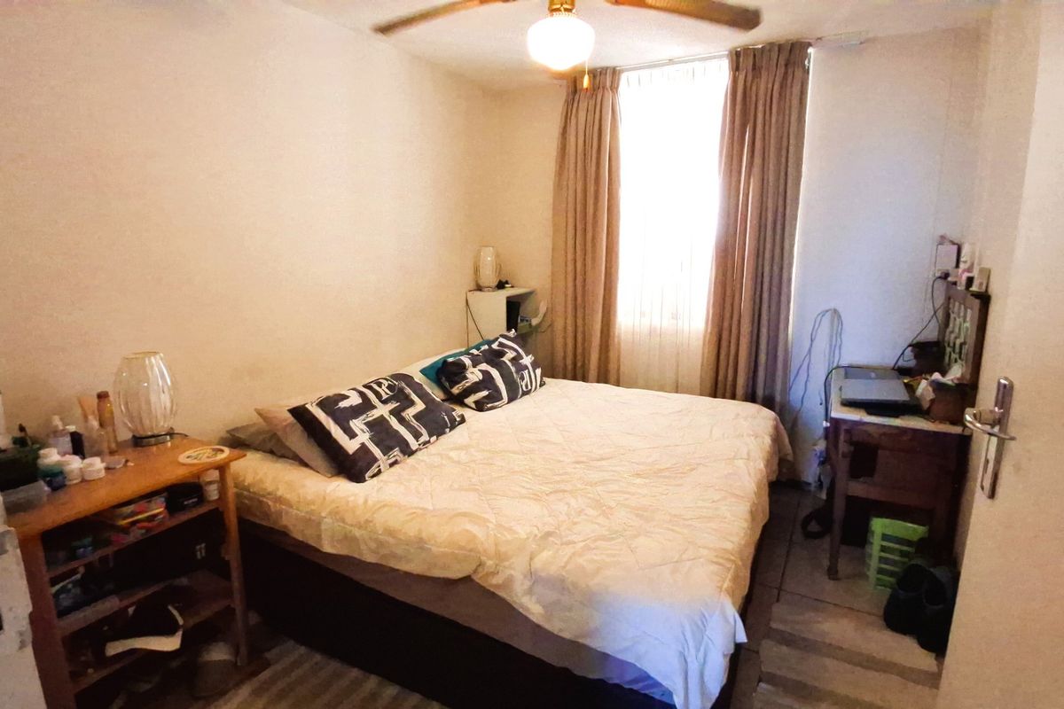 A standard bedroom featuring tiled flooring, a ceiling fan, and a window with curtains, providing a functional sleeping space.
