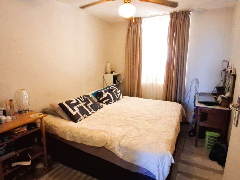A standard bedroom featuring tiled flooring, a ceiling fan, and a window with curtains, providing a functional sleeping space.