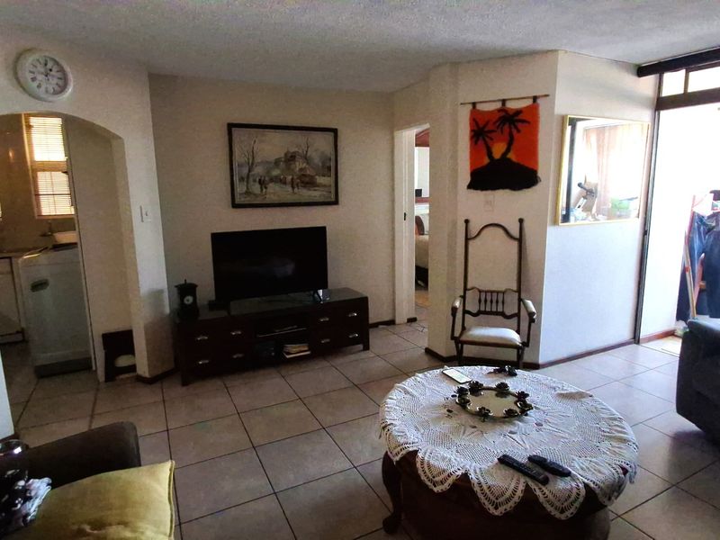 A living room area featuring tiled flooring, an arched entryway to the kitchen, and a sliding glass door leading to an outdoor space.