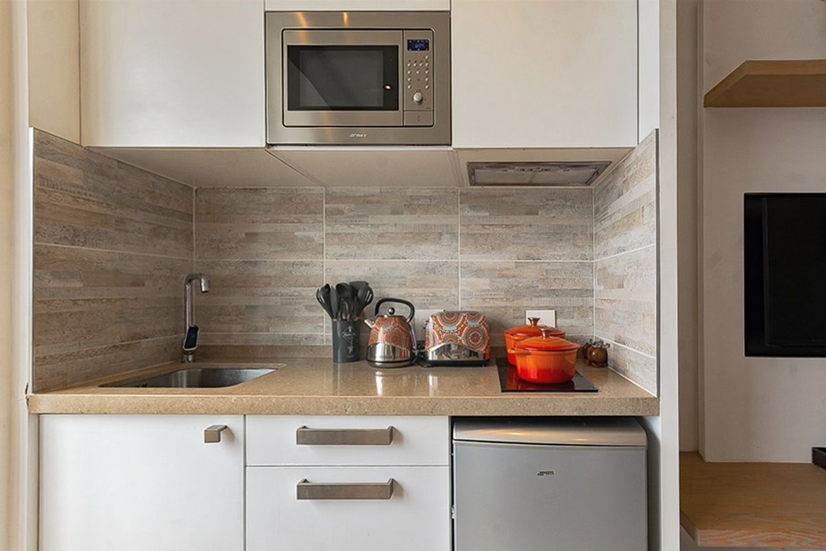 Compact modern kitchen featuring white cabinetry, stone countertops, tiled backsplash, built-in microwave, and integrated hob.
