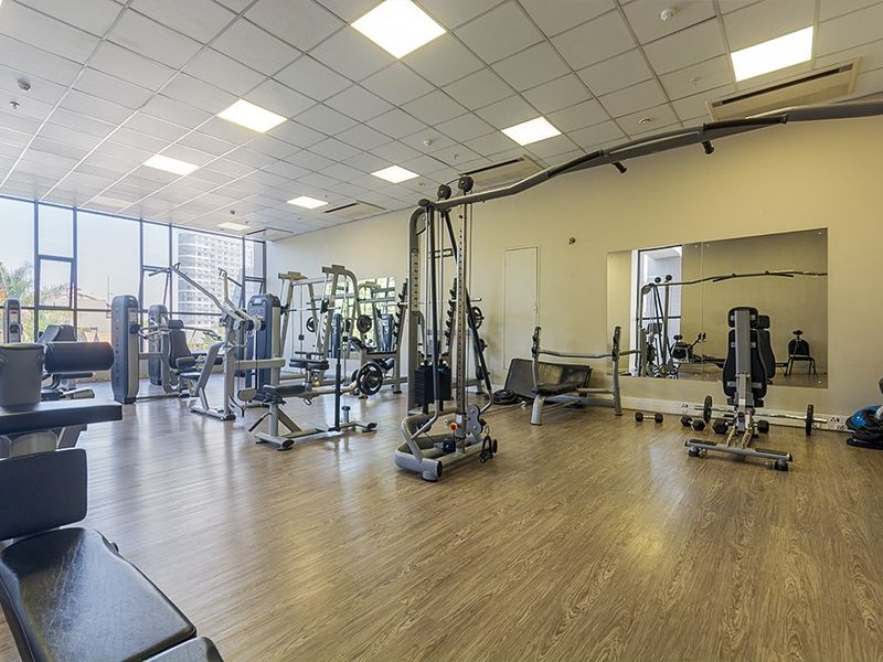 A well-maintained apartment complex gym featuring laminate flooring, floor-to-ceiling windows, wall-mounted mirrors, and integrated ducted air conditioning.
