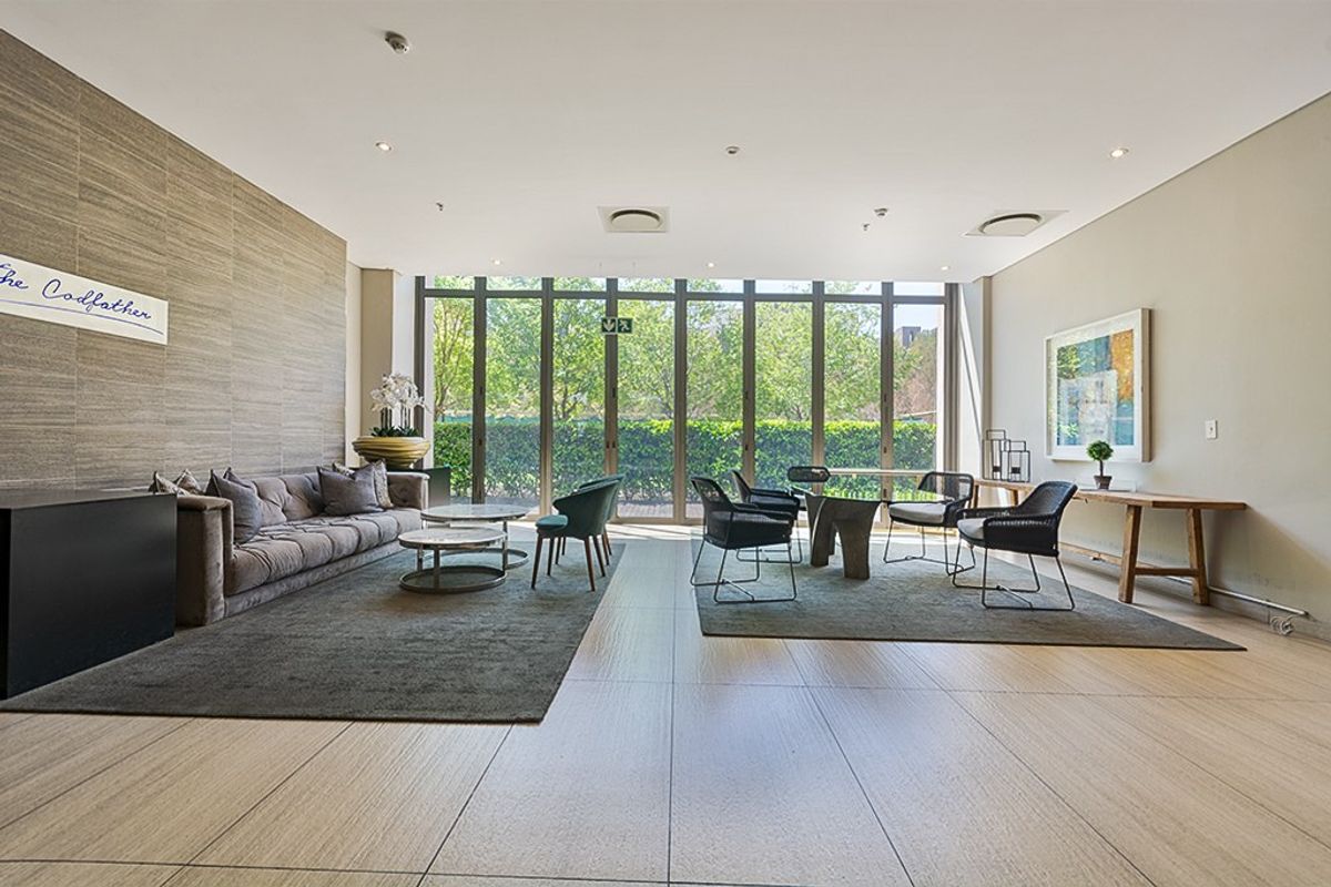 Spacious living area featuring large format floor tiles, a textured feature wall, and floor-to-ceiling glass doors providing ample natural light and garden views.