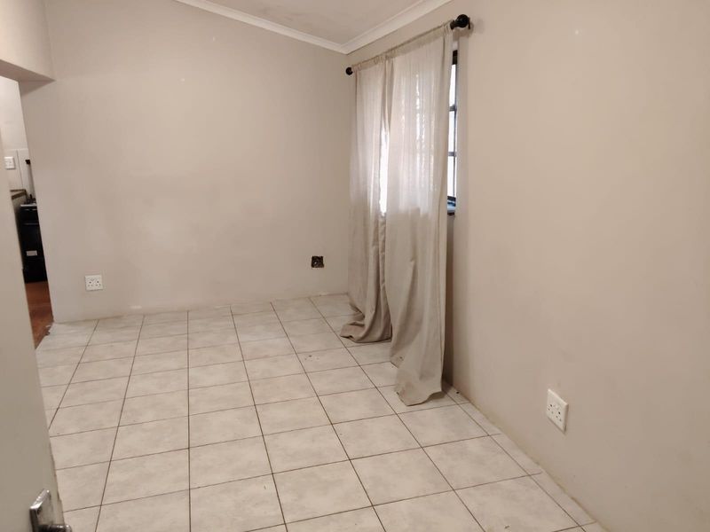 An empty living area featuring tiled flooring, neutral walls, and a window with installed curtain rods.
