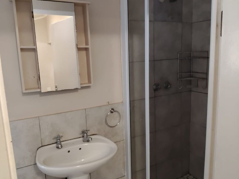 A functional bathroom featuring a pedestal basin, a shower enclosure with tiled walls, and a wall-mounted medicine cabinet.