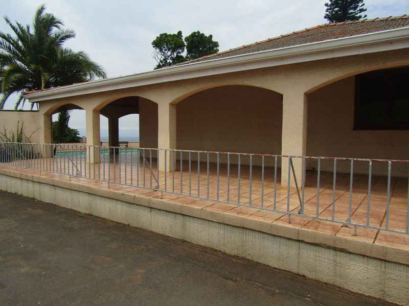 A covered outdoor patio featuring arched masonry columns, tiled flooring, and a metal balustrade, offering a spacious area for outdoor living.