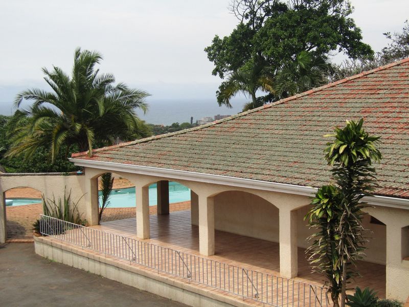 A covered patio area featuring arched pillars and tiled flooring, overlooking a swimming pool with a distant sea view.
