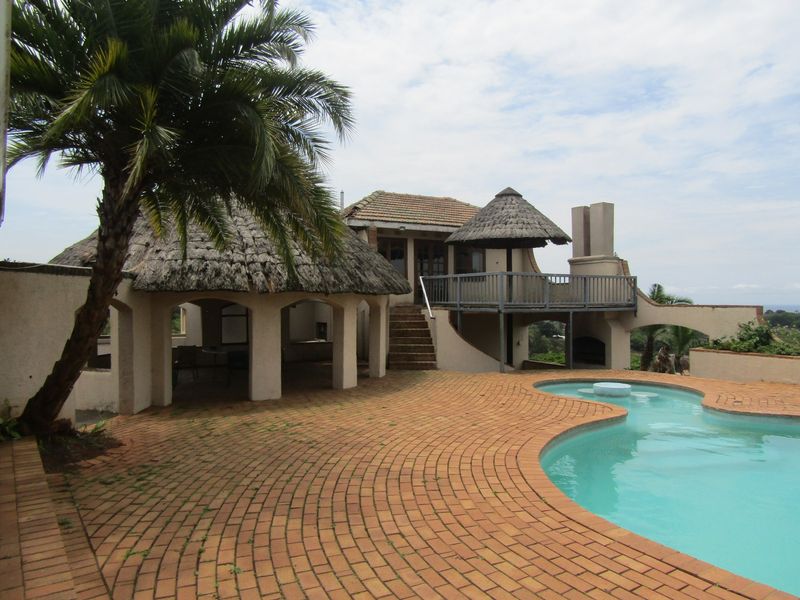 Outdoor entertainment area featuring a swimming pool, brick-paved patio, thatched gazebo, and a raised deck with an integrated fireplace.
