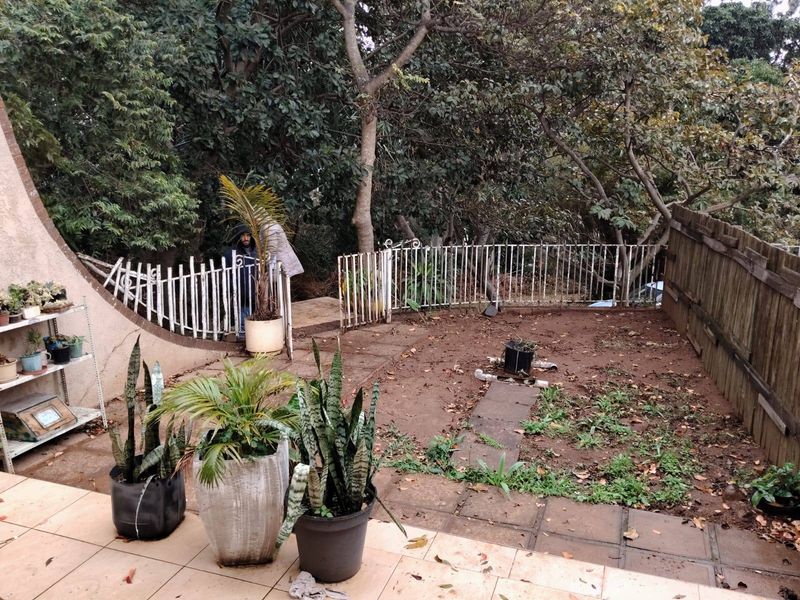 A rear garden area featuring a tiled patio, paved pathway, and perimeter fencing, currently requiring landscaping and maintenance to improve its outdoor appeal.