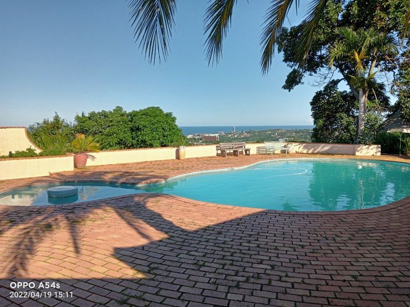 Outdoor pool area featuring a brick-paved deck, retaining wall, and scenic coastal views.