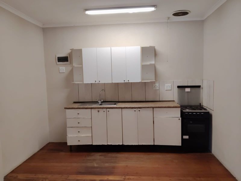 A compact, functional kitchen featuring white cabinetry, a stainless steel sink, a freestanding stove, and timber flooring.