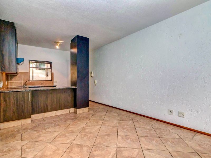 An open-plan living and kitchen area featuring tiled flooring, dark wood-look cabinetry, granite countertops, and a prominent structural column.