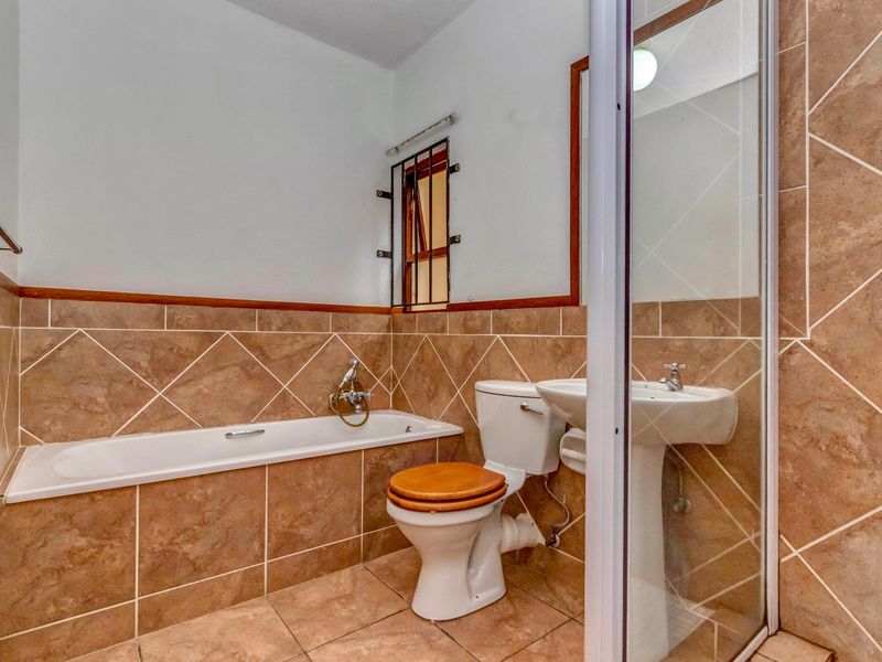 A functional bathroom featuring a bathtub, pedestal sink, toilet, and a separate shower enclosure with brown tiled finishes.