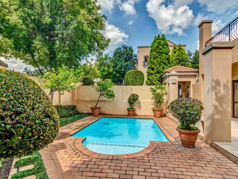 A well-maintained private pool area featuring brick paving, landscaped garden borders, and a tiled patio adjacent to the main building structure.