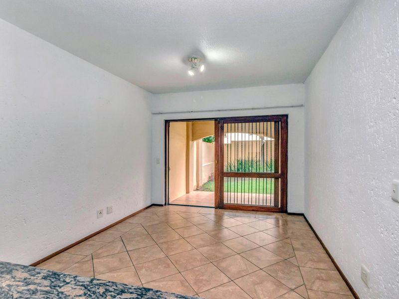 An empty living area featuring tiled flooring and a sliding glass door with a security gate, providing direct access to an outdoor patio space.
