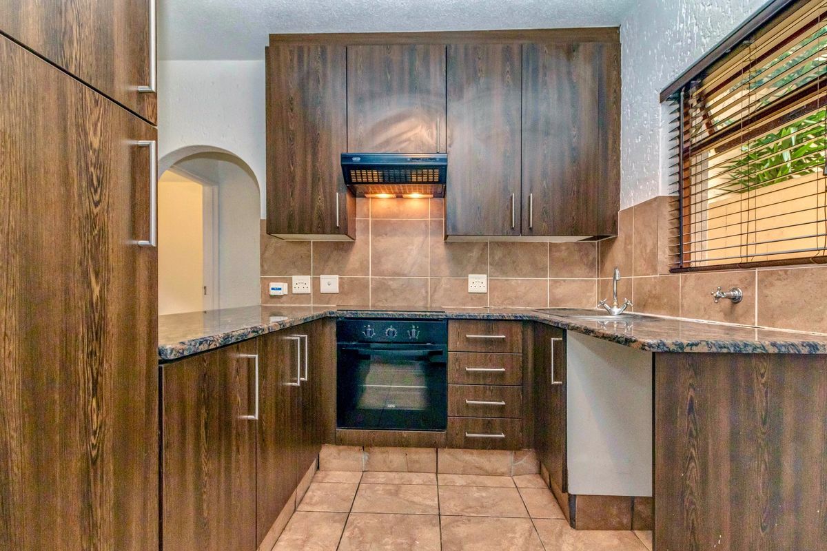 A functional kitchen featuring dark wood cabinetry, granite countertops, a built-in oven with extractor fan, and tiled finishes throughout.