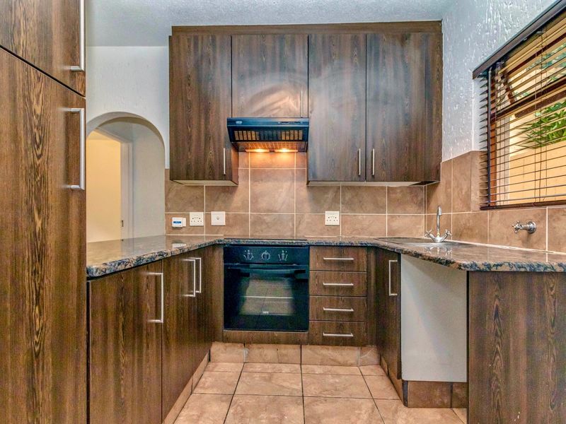 A functional kitchen featuring dark wood cabinetry, granite countertops, a built-in oven with extractor fan, and tiled finishes throughout.