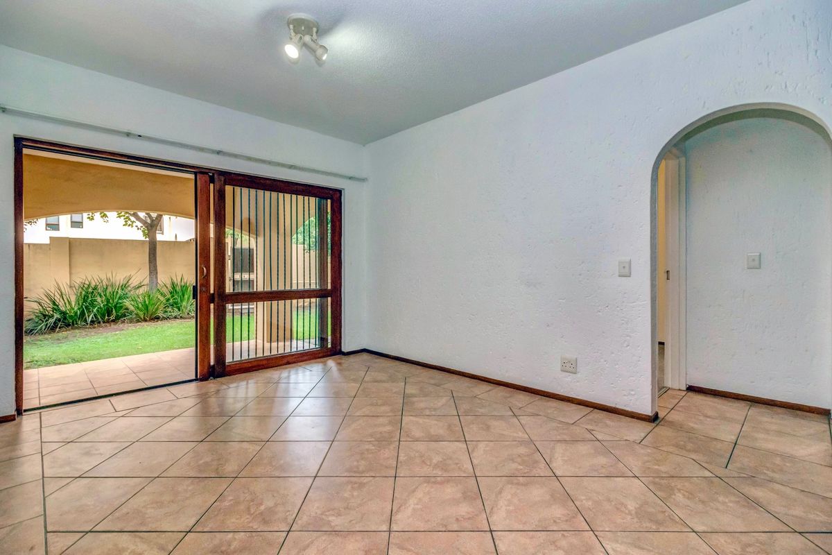 An empty living room featuring tiled flooring, an arched entryway, and a sliding glass door providing access to a private patio and garden area.