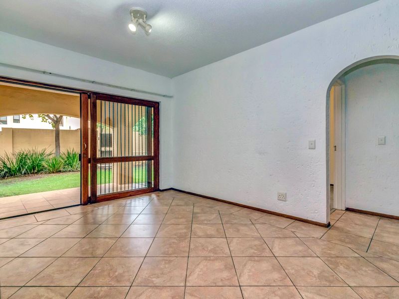 An empty living room featuring tiled flooring, an arched entryway, and a sliding glass door providing access to a private patio and garden area.