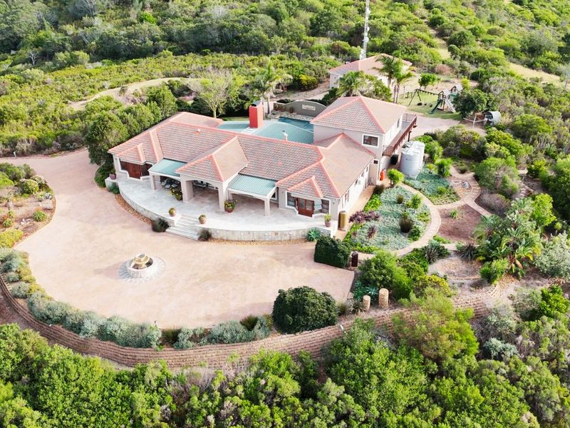 Aerial view of a large residential property featuring a tiled roof, expansive paved driveway, covered patio, and swimming pool set within a landscaped garden.