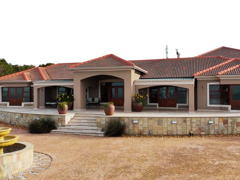 A well-maintained single-story residence featuring a terracotta tile roof, stone-clad retaining wall, paved driveway, and a central stone fountain.