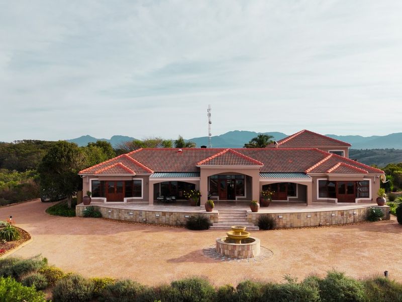 Aerial view of a spacious single-story residence featuring a tiled roof, stone-clad facade, expansive paved driveway, and a central water fountain.