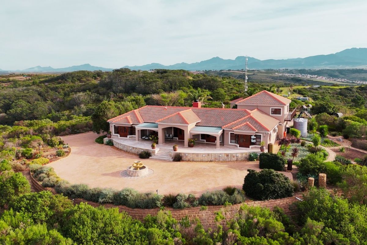 Aerial view of a spacious single-story residence featuring a terracotta roof, expansive driveway, and a stone-walled garden set within a scenic landscape.