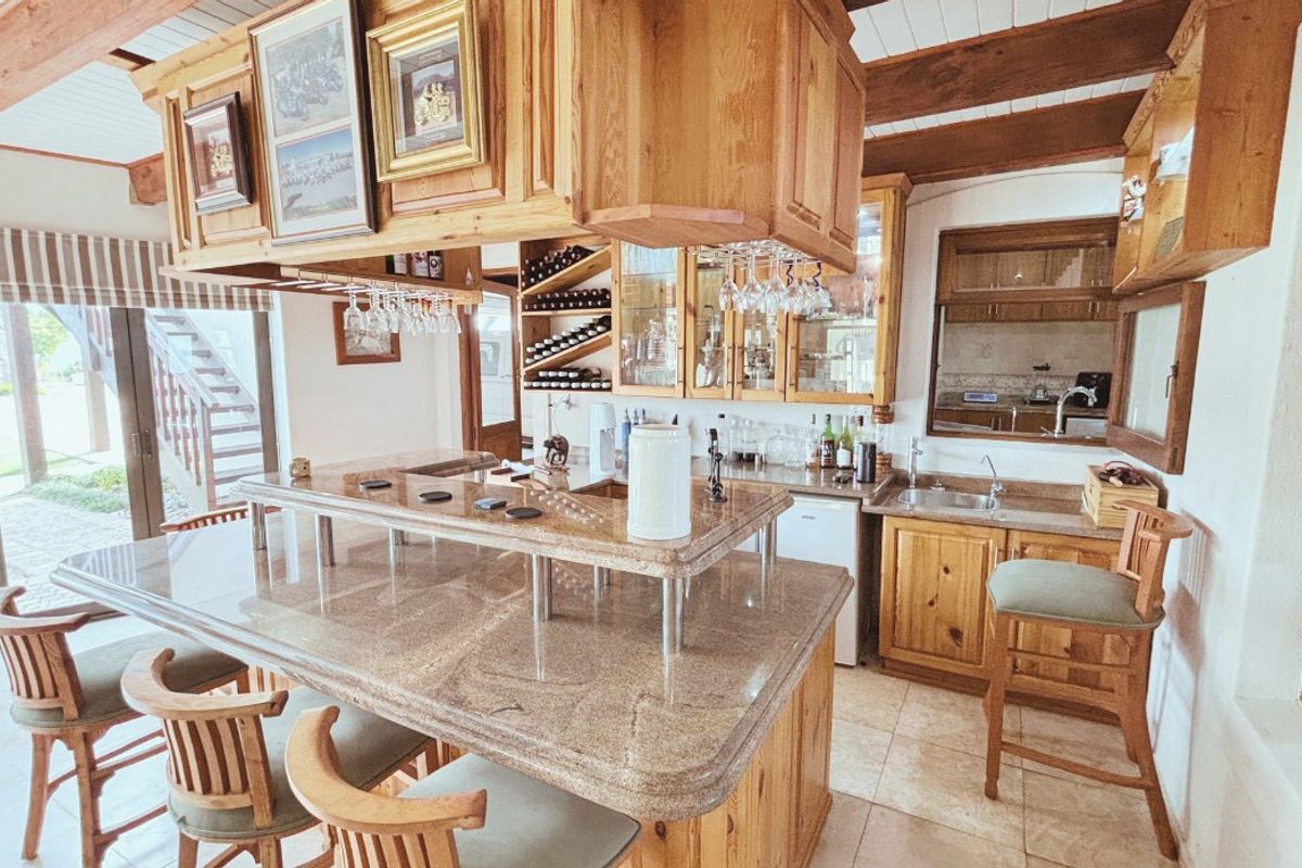 A rustic-style kitchen featuring extensive wooden cabinetry, granite countertops, a breakfast bar, and exposed timber ceiling beams with integrated wine storage.