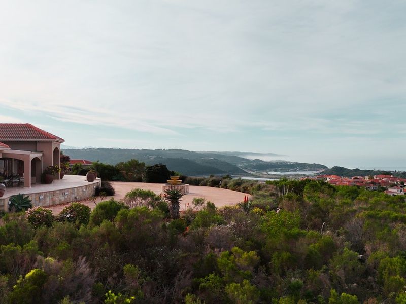 Aerial view of a residential property featuring a spacious paved terrace, stone retaining walls, and expansive coastal landscape views.