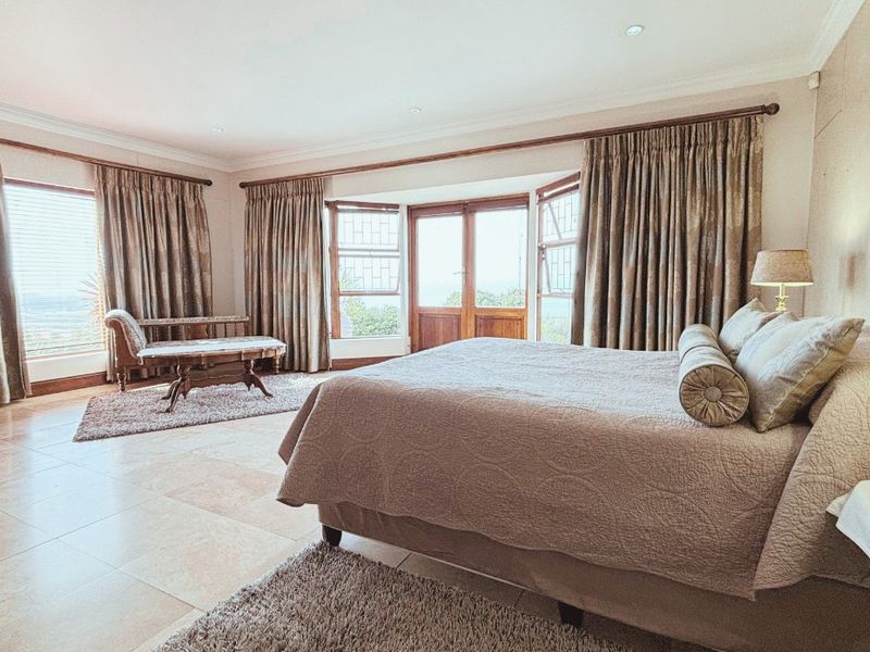 Spacious bedroom featuring large bay windows, tiled flooring, and direct access to an outdoor area through wooden french doors.