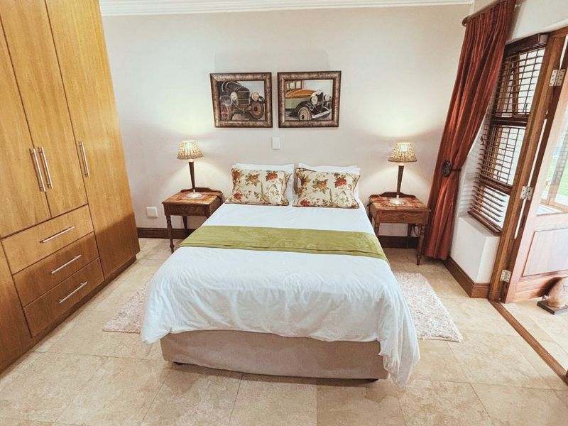 A well-maintained bedroom featuring built-in wooden wardrobes, tiled flooring, and direct access to an outdoor area through a wooden door.
