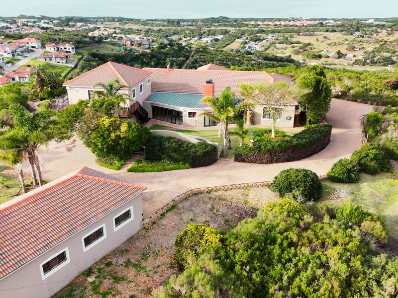 Aerial view of a large residential property featuring a main house with a tiled roof, a detached garage, and extensive landscaped grounds.