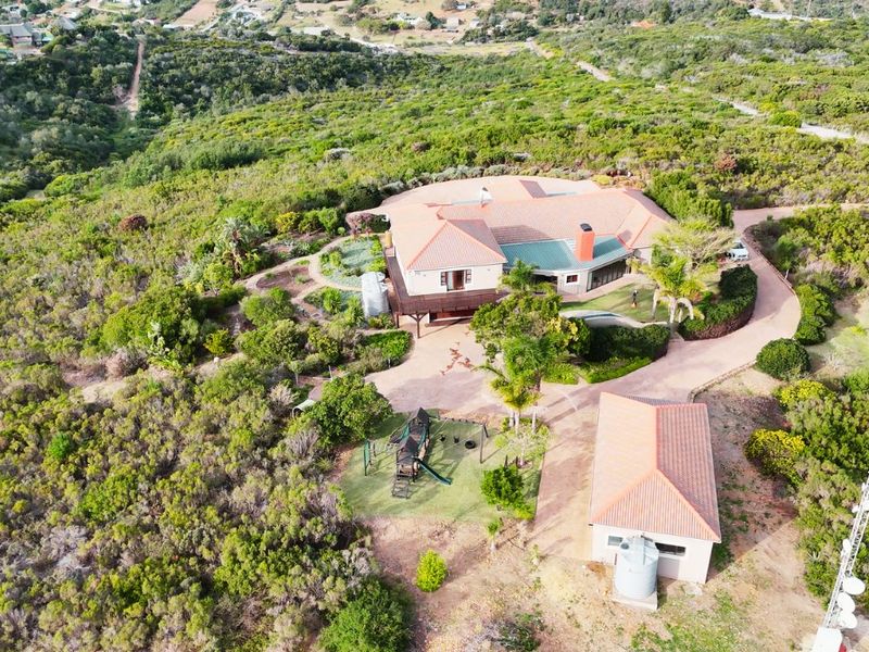 Aerial view of a large residential property featuring a main house with a tiled roof, detached garage, paved driveway, and surrounding natural landscape.