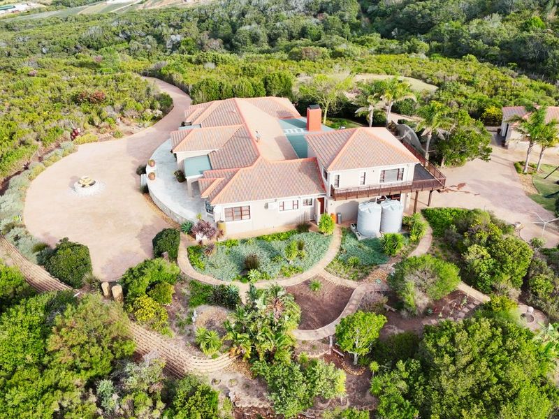 Aerial view of a large residential property featuring a tiled roof, expansive grounds, water storage tanks, and a raised wooden deck.
