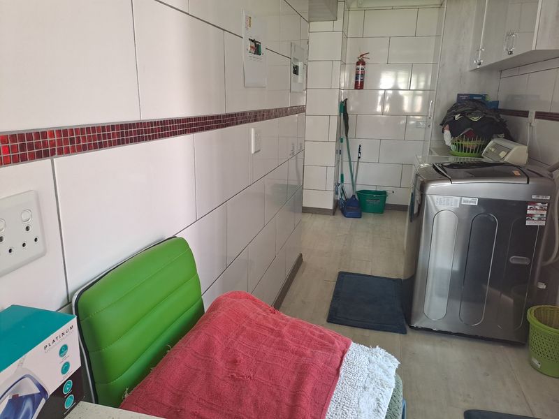 A functional laundry room featuring full-height wall tiling, durable floor tiles, and dedicated space for laundry appliances.