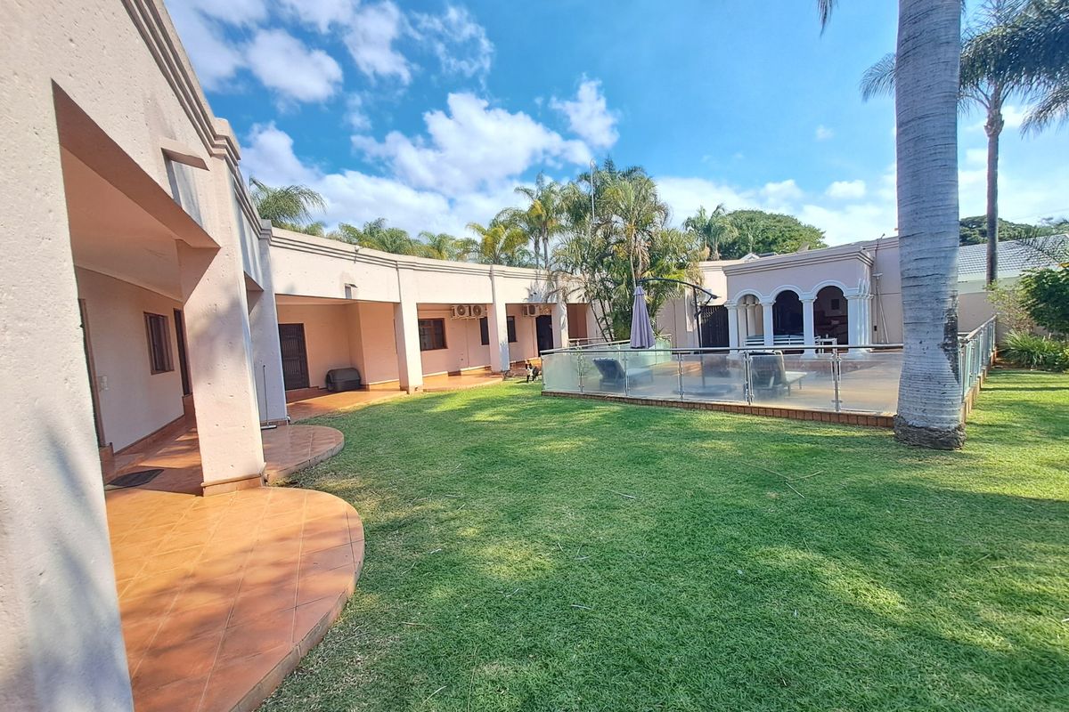 Spacious rear garden featuring a tiled patio area, a swimming pool with a modern glass balustrade, and established landscaping.