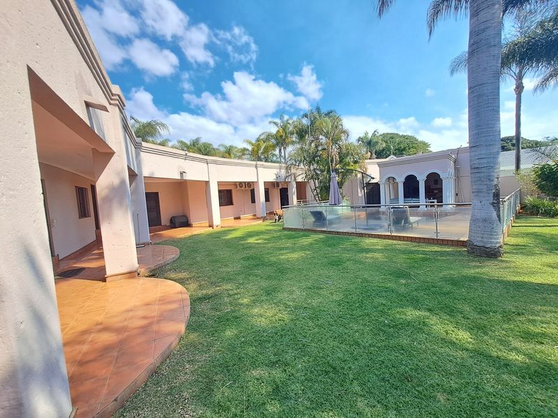Spacious rear garden featuring a tiled patio area, a swimming pool with a modern glass balustrade, and established landscaping.