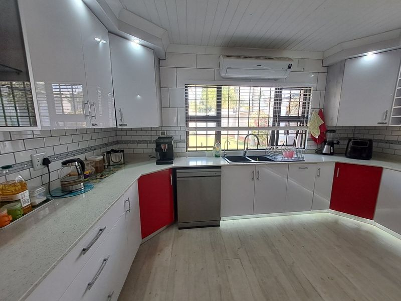 Modern kitchen featuring high-gloss cabinetry, stone countertops, subway tile backsplash, integrated dishwasher, and a split-system air conditioner.
