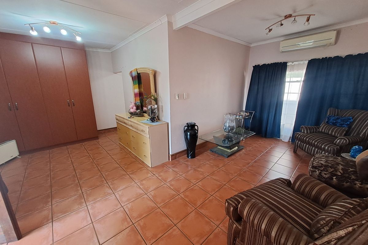 Spacious bedroom featuring tiled flooring, built-in cupboards, and a wall-mounted air conditioning unit.