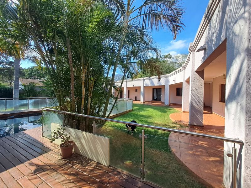 A spacious rear garden featuring a swimming pool, wooden decking, glass balustrades, and a covered tiled patio area.